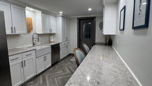 Une cuisine moderne avec des meubles blancs, un plan de travail en marbre et un sol à motifs en chevrons.