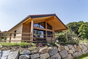 Eine Holzhütte mit geneigtem Dach, großen Fenstern und einer Steinsäule im Vordergrund.
