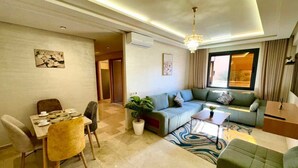 A modern living room with a sofa, dining table, chairs, and a potted plant. - Gueliz Twin Balcony Apartment F3 (Marrakesh)