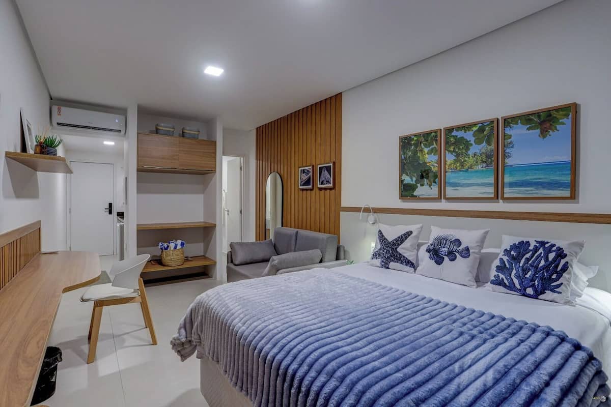 Une chambre moderne avec un lit, un bureau et une chaise. On y trouve deux tableaux encadrés au mur, un miroir et un panneau décoratif en bois.
