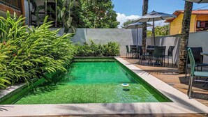 Une piscine rectangulaire bordée de carreaux, entourée d’une végétation luxuriante et dotée d’une terrasse en bois.
