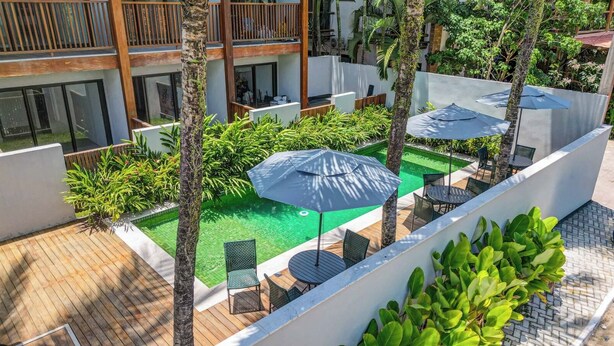 Un espace piscine aménagé sur le toit, avec des chaises longues et des parasols, entouré de verdure et bordé d’une architecture moderne.