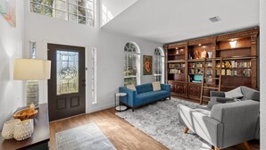 A spacious living room with a large bookshelf, a blue sofa, and a wooden floor. - Family Friendly Hurst Home with Salwater Poo,l Fireplace, and Spacious Layout (Hurst)