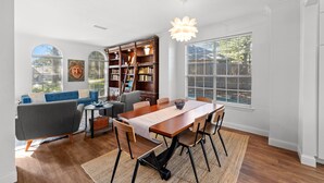 A spacious living room with a large wooden dining table, comfortable seating, a bookshelf, and a large window with blinds. - Family Friendly Hurst Home with Salwater Poo,l Fireplace, and Spacious Layout (Hurst)