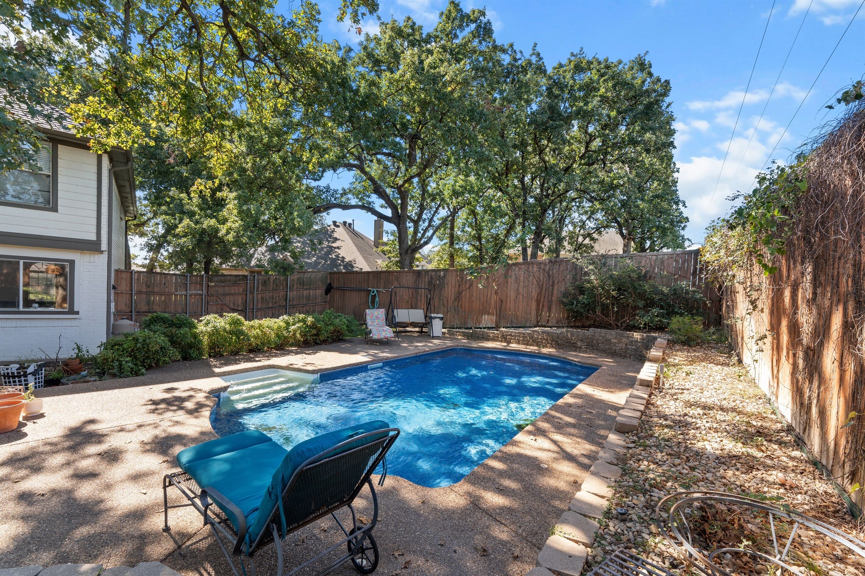 Un patio trasero con piscina, zona de estar techada y cerca de madera.