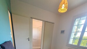 A bedroom with a large bed, a hanging light fixture, a window, and a door leading to a bathroom. - Cosy villa, 6 pers, 800m from the beach, large garden (Fouras)
