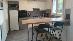 A compact kitchen with a built-in oven, microwave, and gas stove. There are two bar stools and a window providing natural light. - Cosy villa, 6 pers, 800m from the beach, large garden (Fouras)