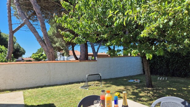 An outdoor patio with a table set for a meal, surrounded by trees and a white wall. - Cosy villa, 6 pers, 800m from the beach, large garden (Fouras)