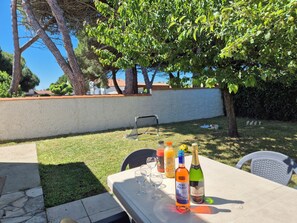 An outdoor patio with a table set for a meal, surrounded by trees and a white wall. - Cosy villa, 6 pers, 800m from the beach, large garden (Fouras)
