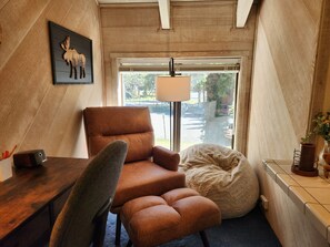 Ein Zimmer mit braunem Ledersessel, einem Schreibtisch mit Lampe, einem großen Fenster mit Blick auf die Straße und einem an der Wand hängenden Bild von einem Elch.
