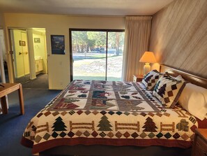 Ein Hotelzimmer mit einem großen Bett, einem Nachttisch, einer Lampe und Blick auf einen Parkplatz durch eine Tür.