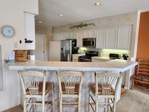 A kitchen with a central island, bar stools, a microwave, and a refrigerator. - Snowcreek Resort Vacation Rental 511 (Mammoth Lakes)