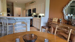 A kitchen with white cabinets, a refrigerator, an oven, and a microwave. There is a dining table with chairs and a decorative mirror. - Snowcreek Resort Vacation Rental 511 (Mammoth Lakes)