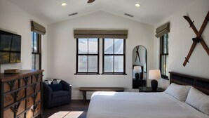 A bedroom with a large bed, a ceiling fan, a bench, a dresser, and a window with a view. - Snowcreek Resort Vacation Rental 1595 (Mammoth Lakes)