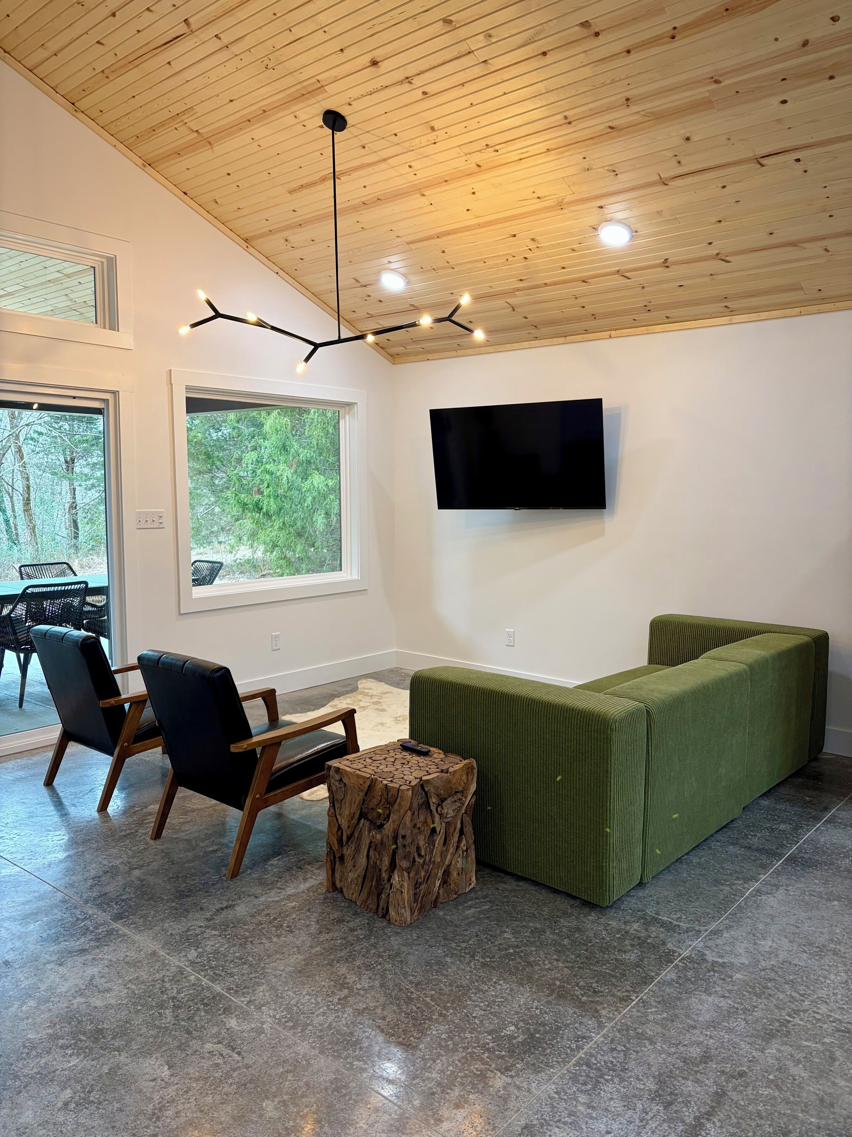 Ein modernes Wohnzimmer mit Holzboden, großem Fenster, Flachbildfernseher und einem grünen Sofa.