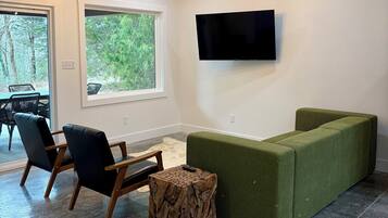 Ein modernes Wohnzimmer mit Holzboden, großem Fenster, Flachbildfernseher und einem grünen Sofa.