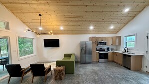 Eine moderne Küche mit Holzausstattung, einem Edelstahlkühlschrank und einem eingebauten Backofen. Es gibt einen Essbereich mit Tisch und Stühlen, sowie ein großes Fenster mit Blick ins Freie.