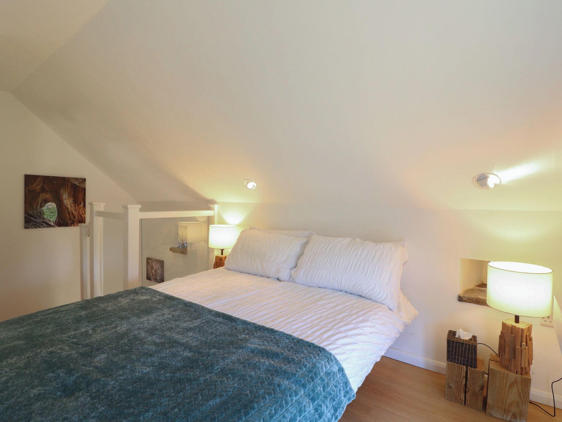 A bedroom with a bed, a nightstand, a lamp, and a painting on the wall.