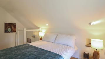 A bedroom with a bed, a nightstand, a lamp, and a painting on the wall.