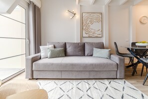 Una sala de estar moderna con un sofá gris, un tapiz estampado, una mesa de comedor con sillas y un reloj de pared.