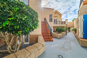 A courtyard with a staircase leading to a building, surrounded by greenery and stone walls.