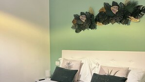 A neatly made bed with white linens and two green pillows, a dark grey bedspread, and a decorative wall hanging above the bed. - Best Stay-Apartments in Andrea da Bari 5 (Bari)