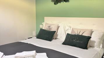 A neatly made bed with white linens and two green pillows, a dark grey bedspread, and a decorative wall hanging above the bed.