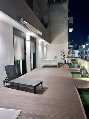 An outdoor patio area with a lounge chair, a small table, and potted plants.