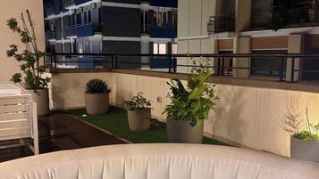 An outdoor seating area with a pool, surrounded by potted plants and a modern building in the background.