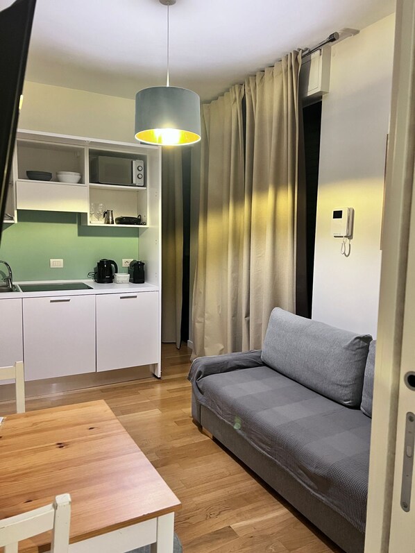 A compact living space with a kitchenette, a sofa, a dining table, and a hanging light fixture.