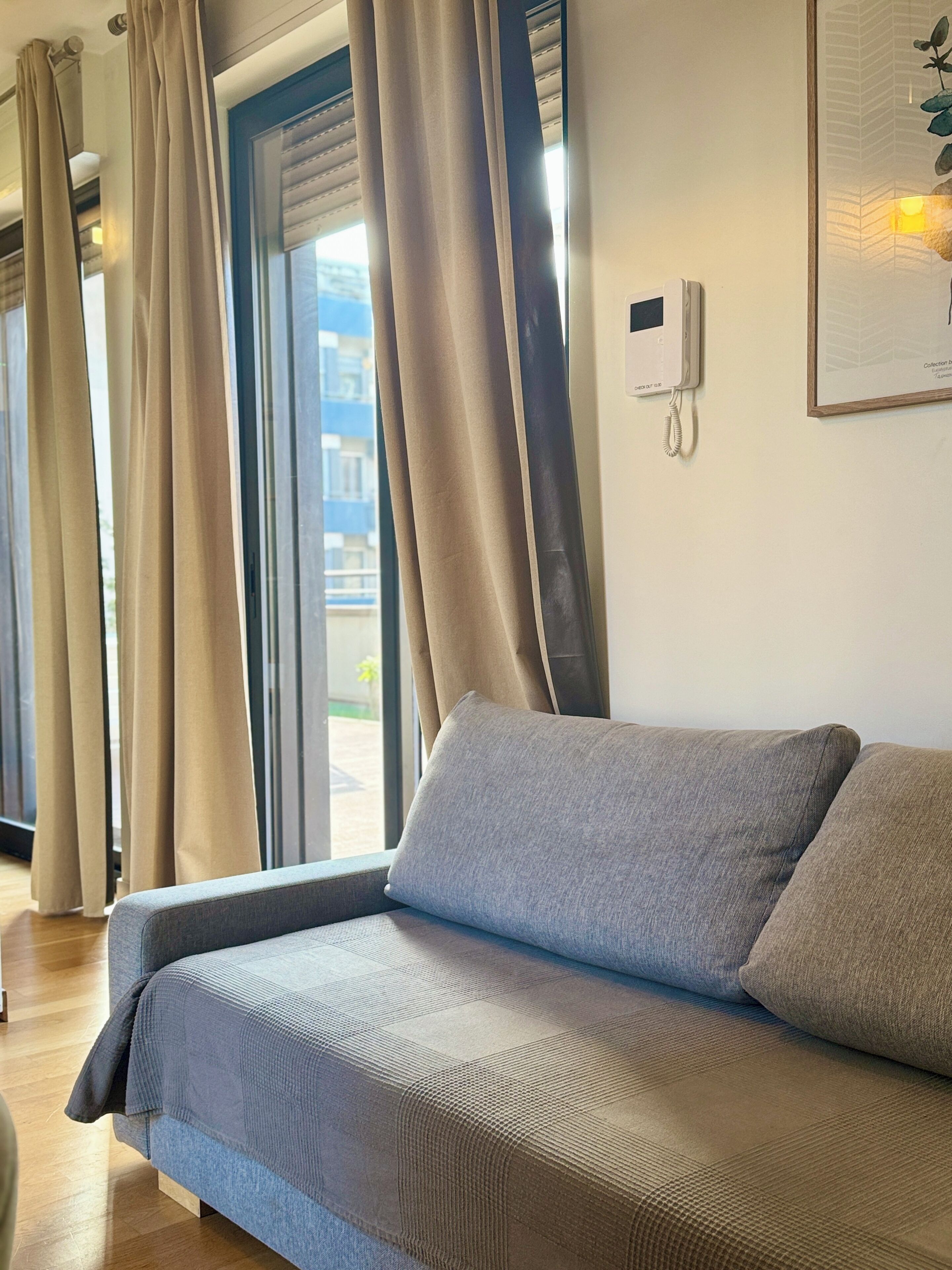 A modern room with a sofa, curtains, a phone, and a framed picture on the wall.