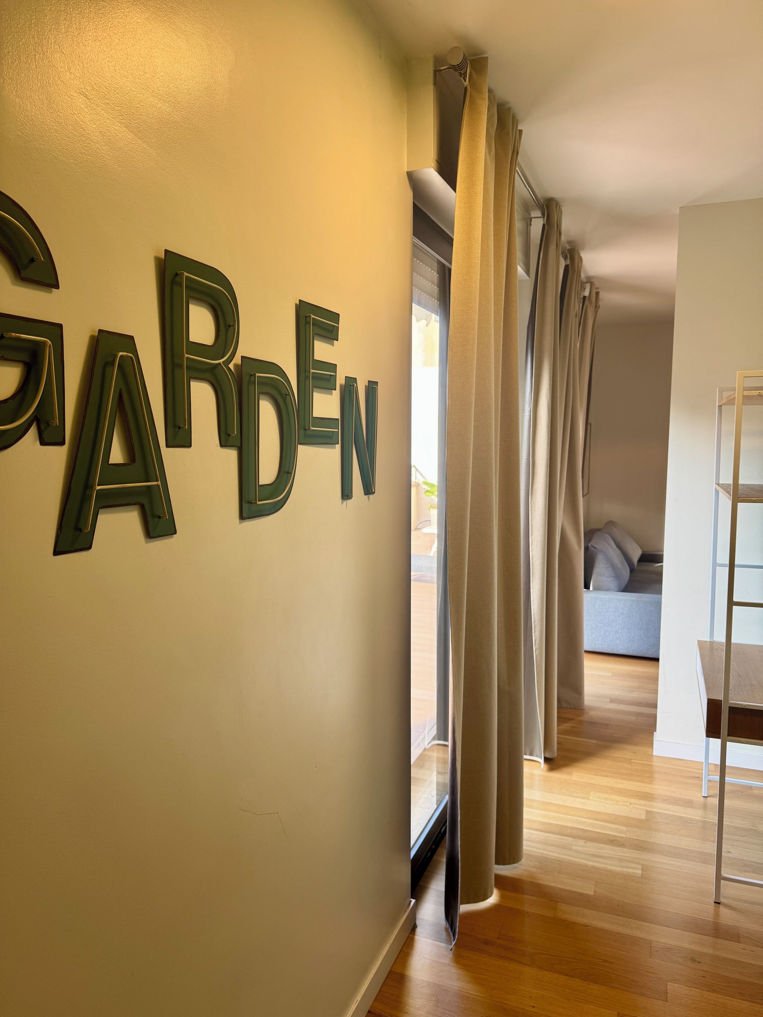 Un pasillo con un letrero que dice "GARDEN" en la pared, que conduce a una habitación con una cama y piso de madera.