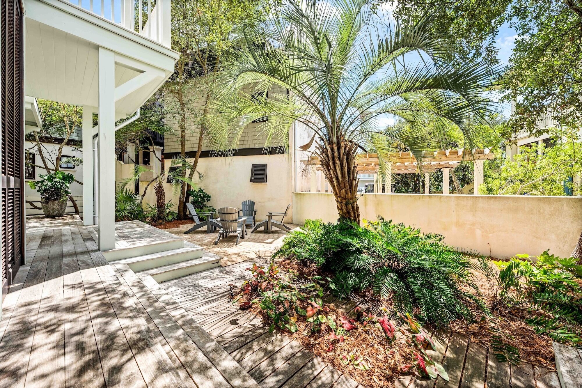 A covered patio with a wooden deck, outdoor seating, and a variety of plants.