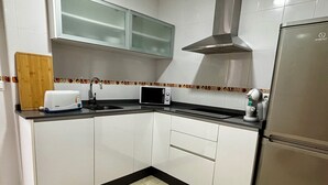 Una cucina con mobili bianchi, un frigorifero in acciaio inossidabile, un forno a microonde e un tostapane.