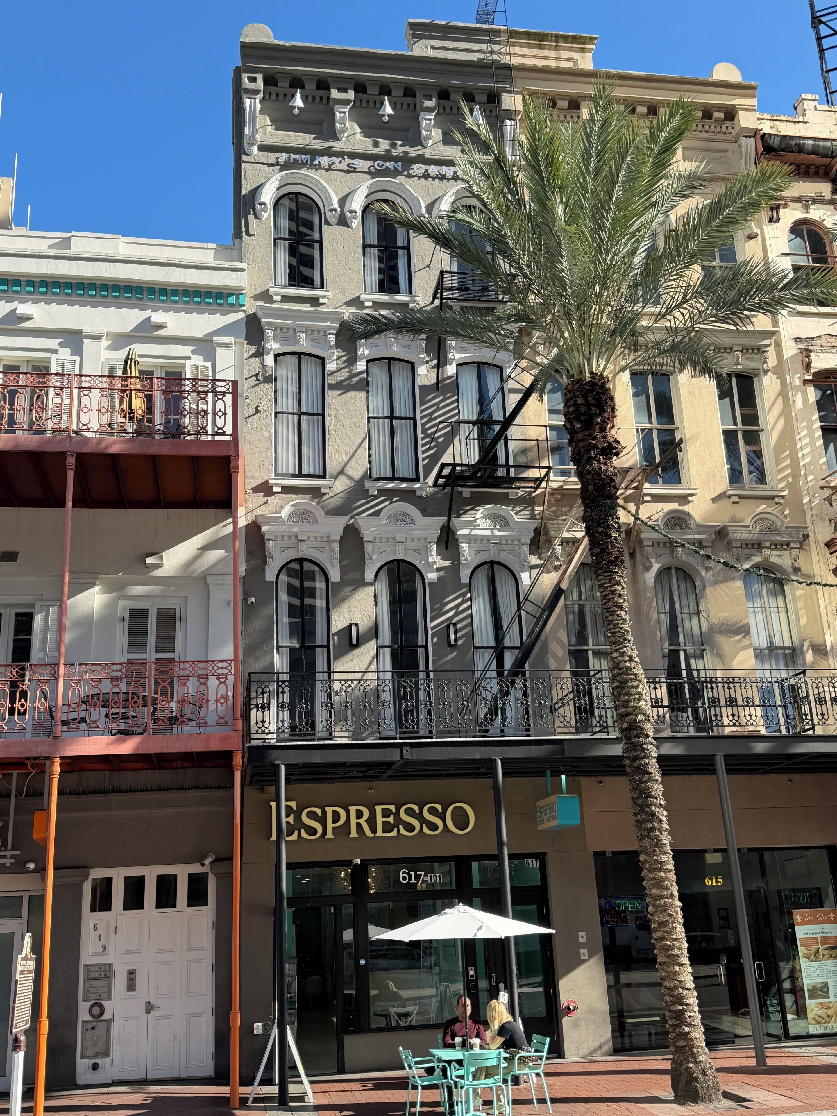 A building with a ground-floor espresso shop, a palm tree, and a red balcony railing.