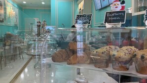 En bageridisplay med forskellige bagværk, blandt andet småkager og kager, med skilte der angiver typer som 'Raspberry Muffin' og 'Almond Croissant'.