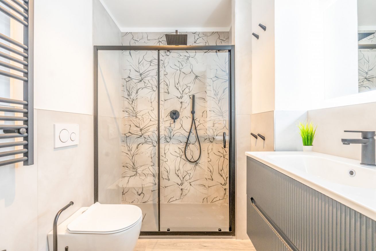 A modern bathroom with a glass shower enclosure, a white toilet, and a large sink with a mirror.