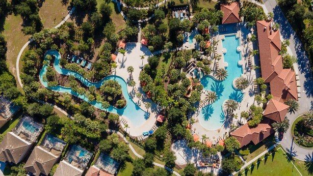 Eine Vogelperspektive zeigt ein Resort mit mehreren Schwimmbecken, Palmen und einem Tennisplatz.