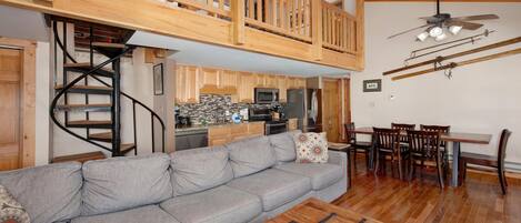 A spacious living area with a grey sofa, wooden dining table, and a spiral staircase leading to a loft.