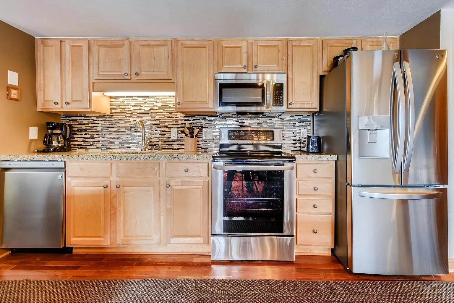A modern kitchen with wooden cabinets, stainless steel appliances, a tiled backsplash, and a built-in oven.
