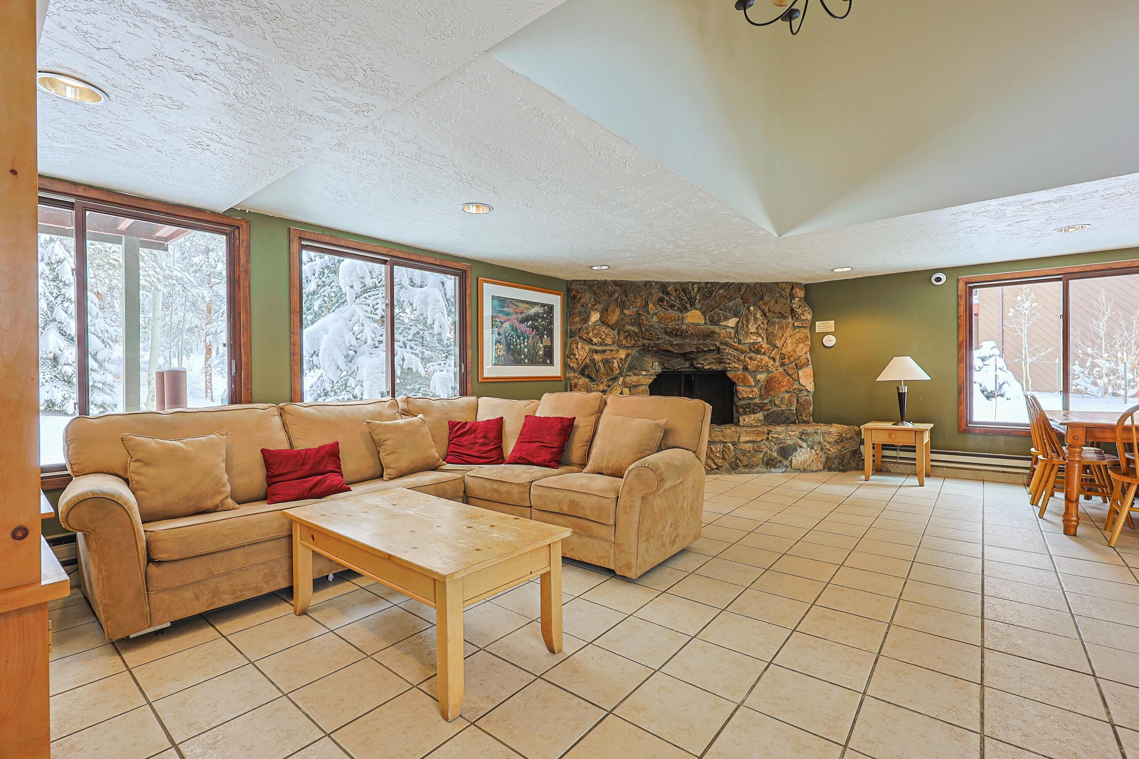 A living room with a stone fireplace, a sofa set, a wooden coffee table, and a dining area with chairs and a table.