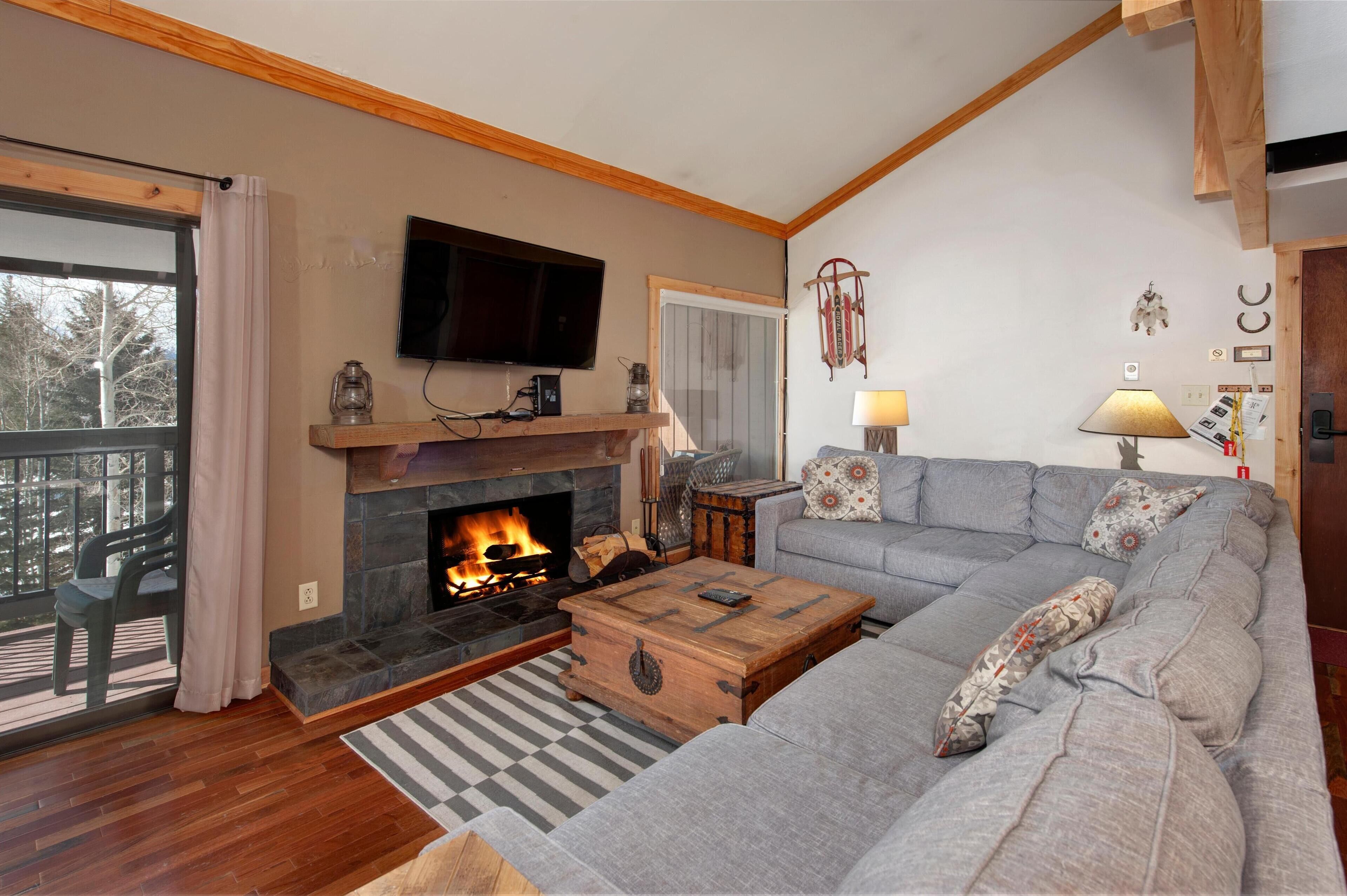 A living room with a fireplace, a sofa, a television, and a window with a view of trees.