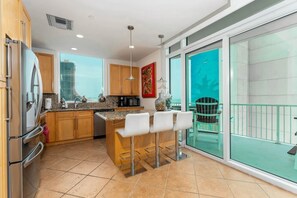 A modern kitchen with granite countertops, stainless steel appliances, and a central island with bar stools. - Sapphire 601 - By GISO Vacation Rentals (South Padre Island)