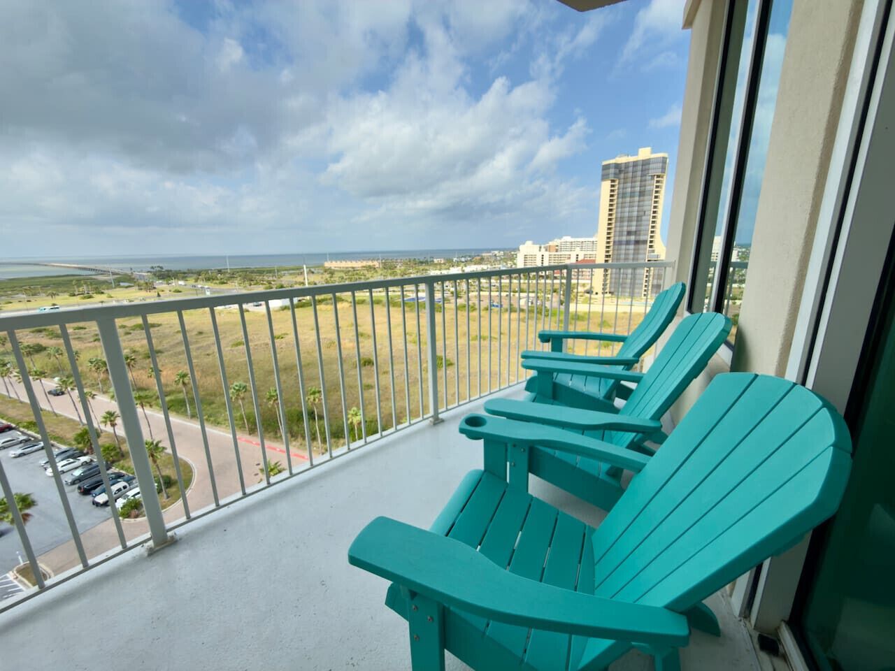 Een balkon met smaragdgroene Adirondack-stoelen, met uitzicht op een parkeerplaats en een verre hoge wolkenkrabber.