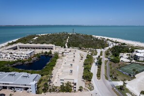Vue aérienne d’une propriété située sur la côte, avec une plage, un court de tennis et un espace de stationnement.