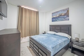 Ein Schlafzimmer mit einem Bett, einem Nachttisch, einer Lampe, einem Bild an der Wand und einem Vorhang.