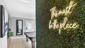 Ein moderner Innenraum mit Billardtisch, einer Neon-Leuchtreklame mit dem Schriftzug „This must be the place“ und einer mit Grünpflanzen bewachsenen Wand.