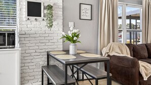 Ein modernes Wohnzimmer mit einer weißen Ziegelwand, einem Esstisch mit zwei Stühlen, einem braunen Ledersofa und einem Fenster mit Vorhängen.