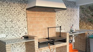 Un área de cocina exterior con mostrador de ladrillo, una parrilla empotrada y un lavamanos.