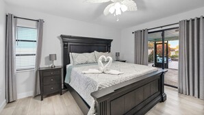 Ein Schlafzimmer mit einem Bett, einem Nachttisch, einer Lampe, einem Deckenventilator und Blick ins Freie.